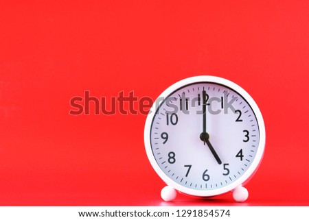 White clocks tell us about 5 o'clock, wooden table, and red background.