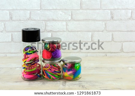 Glass jars filled with craft supplies with a white brick background