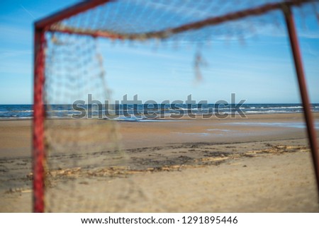 view of the sea beach through the old, broken football goal, the grid is torn close-up, sunny weather, the sky without clouds