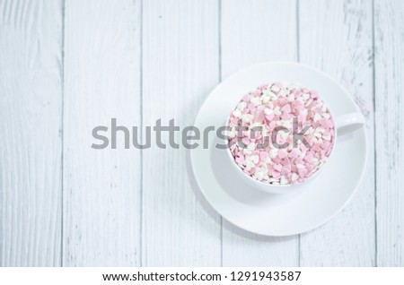 White coffee cup on wooden floor.Many small hearts, white and pink, are in a cup of coffee.Pink square wood with 1 and 4 white numbers, white glass.
