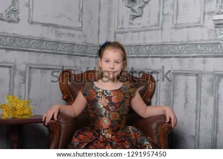 blonde child girl in a golden dress with a flower pattern sits in a vintage chair