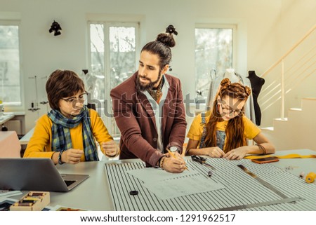 With hair bun. Dark-haired bearded designer with hair bun working near his stylish cute children