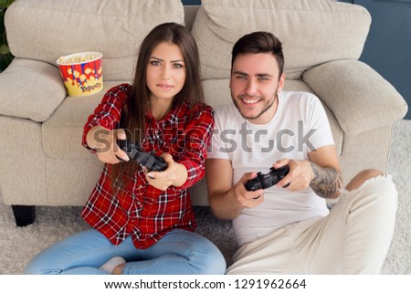 Play games together! Top view portrait of wonderful smiling young people sitting on the floor and leaning the sofa, while playing set-top box.