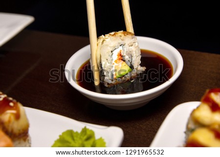 closeup man eating delicious sushi with two chopsticks with food in the background