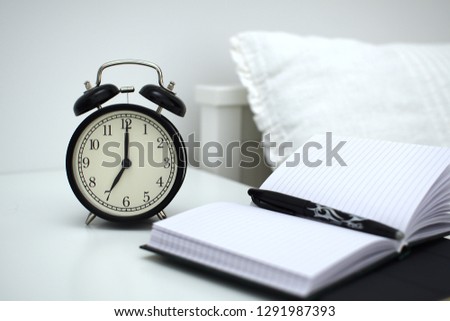 Alarm clock on table with notebooks and pen. Wake up concept. An image of a alarm clock showing 07:00 am.                                                               