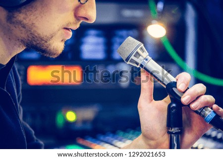 Young man is sitting in the recording studio and talks into the microphone, buttons and equipment in the blurry background