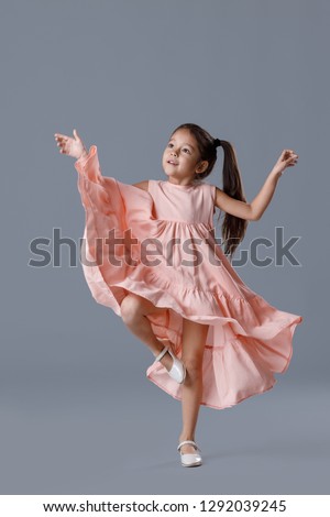 cute smiling little child girl in pink dress dancing on gray background.