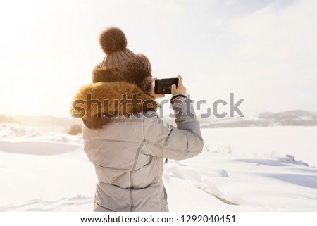 woman is photographing on the phone a snow-covered field