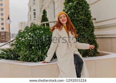 Dreamy red-haired woman posing on the street in winter day. Outdoor photo of merry caucasian girl expressing positive emotions.