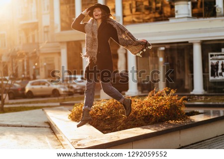 Emotional girl in trendy black hat jumping on city background. Blithesome european female model posing in coat.