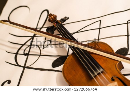 Close up of Violin handle with bow  positioned in a diagonal over a horizontal musical stave drawing with a G-clef with musical notes on a white background
