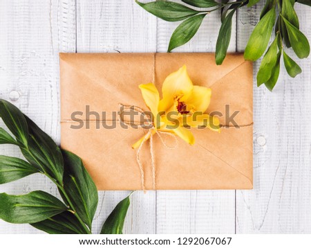 Eco paper envelope with yellow orchid flowers and green leaves on white wooden background. Wedding invitation cards or love letter. Valentine's day or other holiday concept, top view, flat lay
