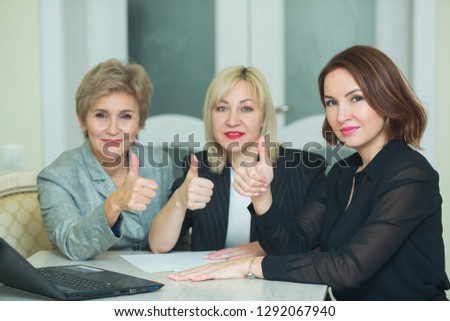 three adult women in suits are sitting at the table with a laptop at work in the office with a gesture of hands