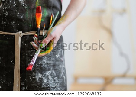 Woman artist's hand with a brush and red paint. Black apron, white background in the art studio. Copy space.