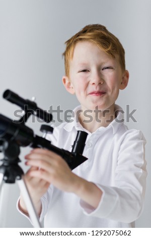 Kid looks through a telescope at the starry sky and smiles. Gray background.