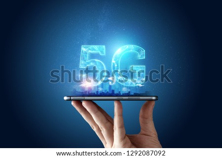 Creative background, male hand holding a phone with a 5G hologram on the background of the city. The concept of 5G network, high-speed mobile Internet, new generation networks. Mixed media. Royalty-Free Stock Photo #1292087092