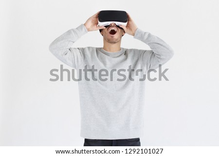 Astonished young man experiencing virtual reality while using VR headset for entertaining. People, technology and innovation concept. 