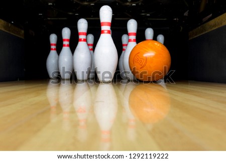orange bowling ball and white skittles stand on a wooden bowling alley. copy space