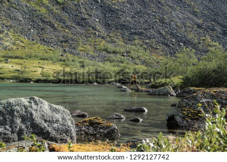 Young male tourist photographs a beautiful transparent lake with moss covered stones on a background of mountains