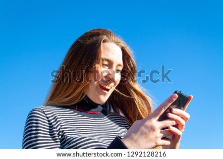 Happy girl with brown hair talking on the phone in the country in the summer. Portrait of the young woman with a black phone and sunlight shining on her hair. - Image