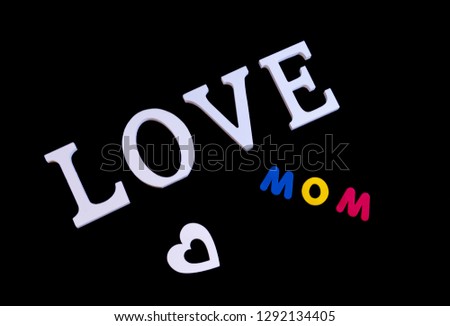 Overhead picture of white word love, white heart and colored word mom, in black background