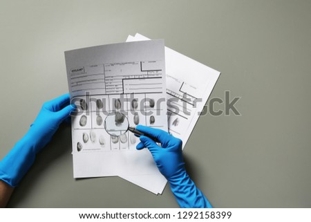 Criminologist exploring fingerprints with magnifier on grey background
