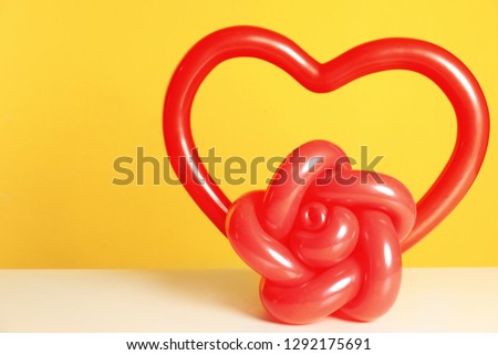 Rose and heart figures made of modelling balloons on table against color background. Space for text