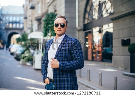 Portrait of a young handsome man, model of fashion, wearing tinted sunglasses in urban background.