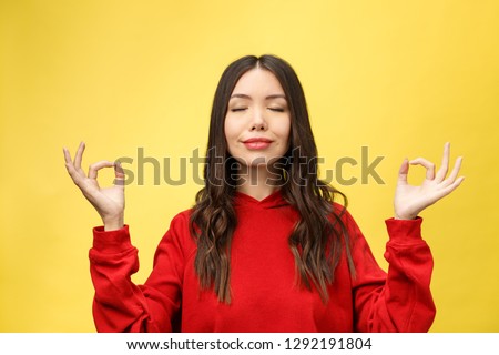 People, yoga and healthy lifestyle. Gorgeous young woman dressed in light red sweater keeping eyes closed while meditating indoors, practicing peace of mind, keeping fingers in mudra gesture