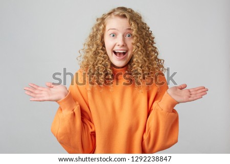 curly blonde very happy with the words of her girlfriend, depicts surprise, eyes and mouth are wide open, hands raised with palms up, a pleasant surprise, great news
