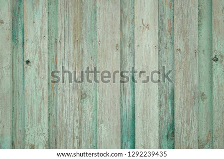 Background old wooden fence. Old faded fence with remnants of peeling paint green, alternating darker and lighter green vertical boards.