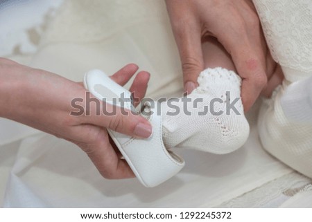 
Hands of a mother putting the little shoe on her baby on her foot for her christening