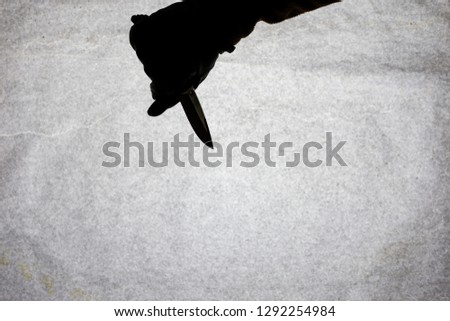 The knife in the hand of men who is ready to attack his victim. Breaking the law and crime. Attack with a knife. Silhouette on a light background.