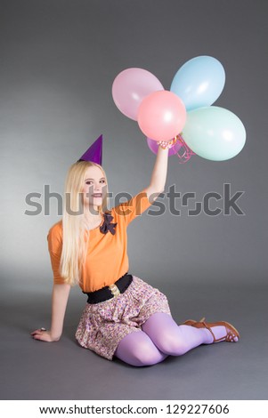 young beautiful blond sitting over grey background with balloons