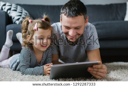 Happy father and daughter lying on the floor and using tablet at home