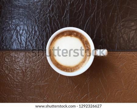 Top view picture of a white cup of cappuccino on brown leather texture.