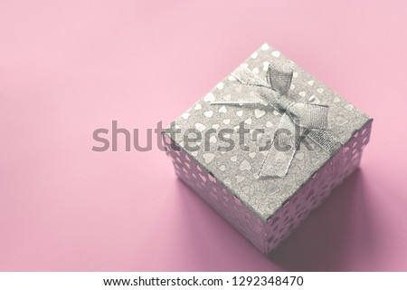 Festive picture of silver gift box with a bow and small hearts on the gentle pink background. Holiday atmosphere. Sent Valentine's day and wedding holiday's concept.