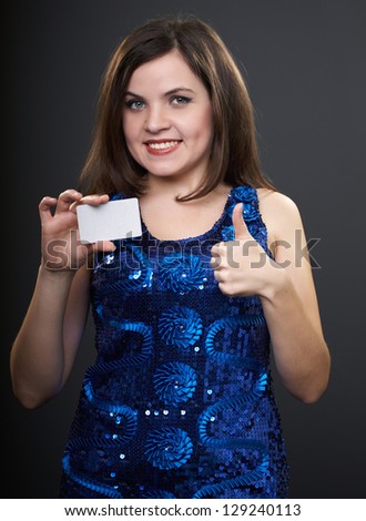 Attractive young woman in a blue dress. Woman holds a poster in her right hand. Left hand showing thumbs up. On a gray background