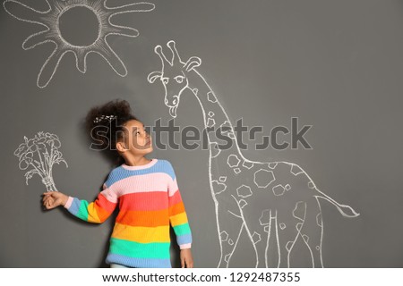 African-American child playing with chalk drawing of giraffe and flowers on grey background
