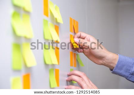 IT worker tracking his tasks on kanban board. Using task control of agile development methodology. Man attaching sticky note to scrum task board in the office Royalty-Free Stock Photo #1292514085