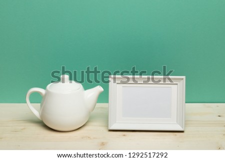 white frame with teapot on  desk near green wall