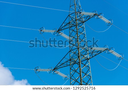 High voltage tower (power line) with electric cables and insulators, on a blue sky with clouds