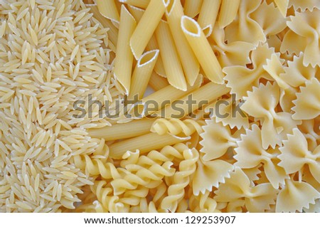 Risoni, penne, farfalle and fusilli. Italian cuisine pasta food varieties background. Royalty-Free Stock Photo #129253907