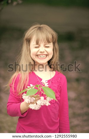 small baby girl or cute child with adorable smiling face and blonde hair in pink shirt holding spring sakura flower, cherry blossom outdoor on blurred background