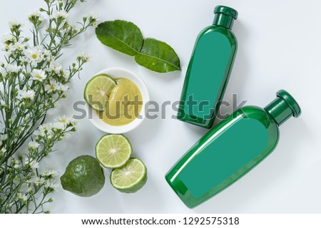 natural products for hair concept. two size of green plastic bottle with blank label contain herbal bergamot shampoo decorate with slide kaffir limes ,kaffir leaf and white flowers on white background Royalty-Free Stock Photo #1292575318