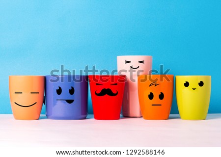 A lot of multi-colored cups with funny faces on a blue background. The concept of a friendly company, a big family, meeting friends for a cup of tea or coffee, father's day, office, boss day. Royalty-Free Stock Photo #1292588146