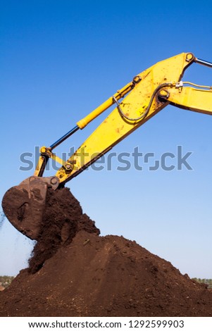 Construction mechanical excavator with a large hydraulic bucket works on the construction site digging a trench and pouring out the soil