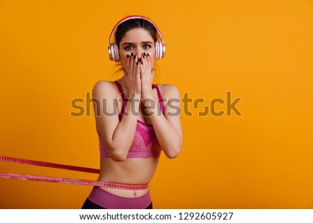 Adorable young woman in headphones measuring her waistline. Sporty caucasian girl posing on yellow background.