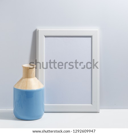Mock up white frame and blue vase on book shelf or desk. White-blue colors. Minimalistic concept.