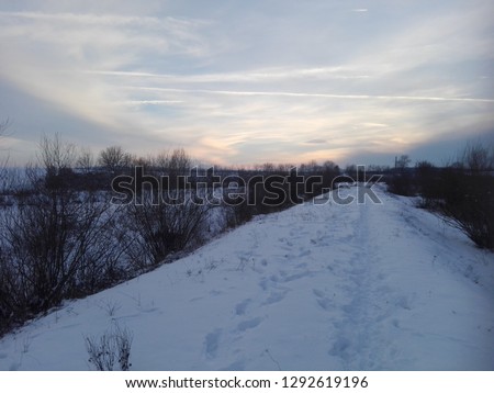 winter sunset over a snowy road near a river shore
